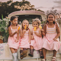 Four young girls sitting on a car's trunk, wearing pink dresses with a ombre popsicle print, and enjoying popsicles.