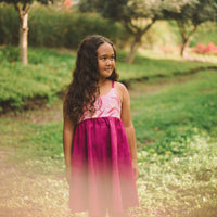 A young girl wearing a pink tropical print dress with a twirly skirt standing in a garden setting.