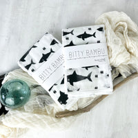A black and white baby burp cloth with shark patterns, displayed alongside a cloth diaper and a glass ornament, presented on a neutral background.