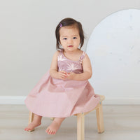 Girl wearing the 'Bird of Paradise' dress, showcasing the full skirt and sitting on a chair