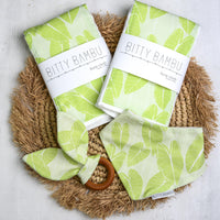 Two packages of Bitty Bambu baby cloths with green leaf pattern on a woven mat.