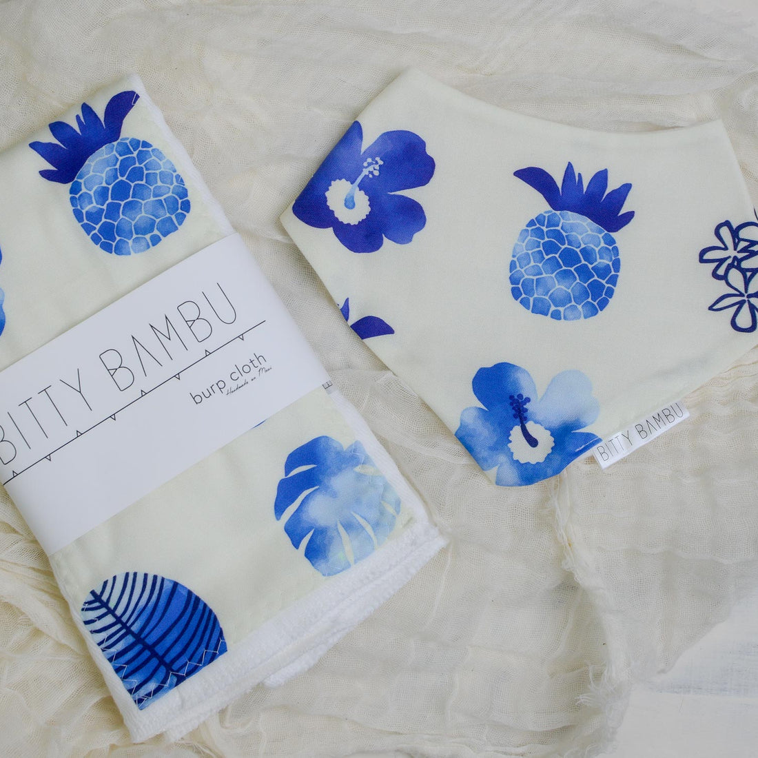 A burp cloth and baby bib with blue floral patterns on a white surface, featuring the brand 'Bitty Bambu'.
