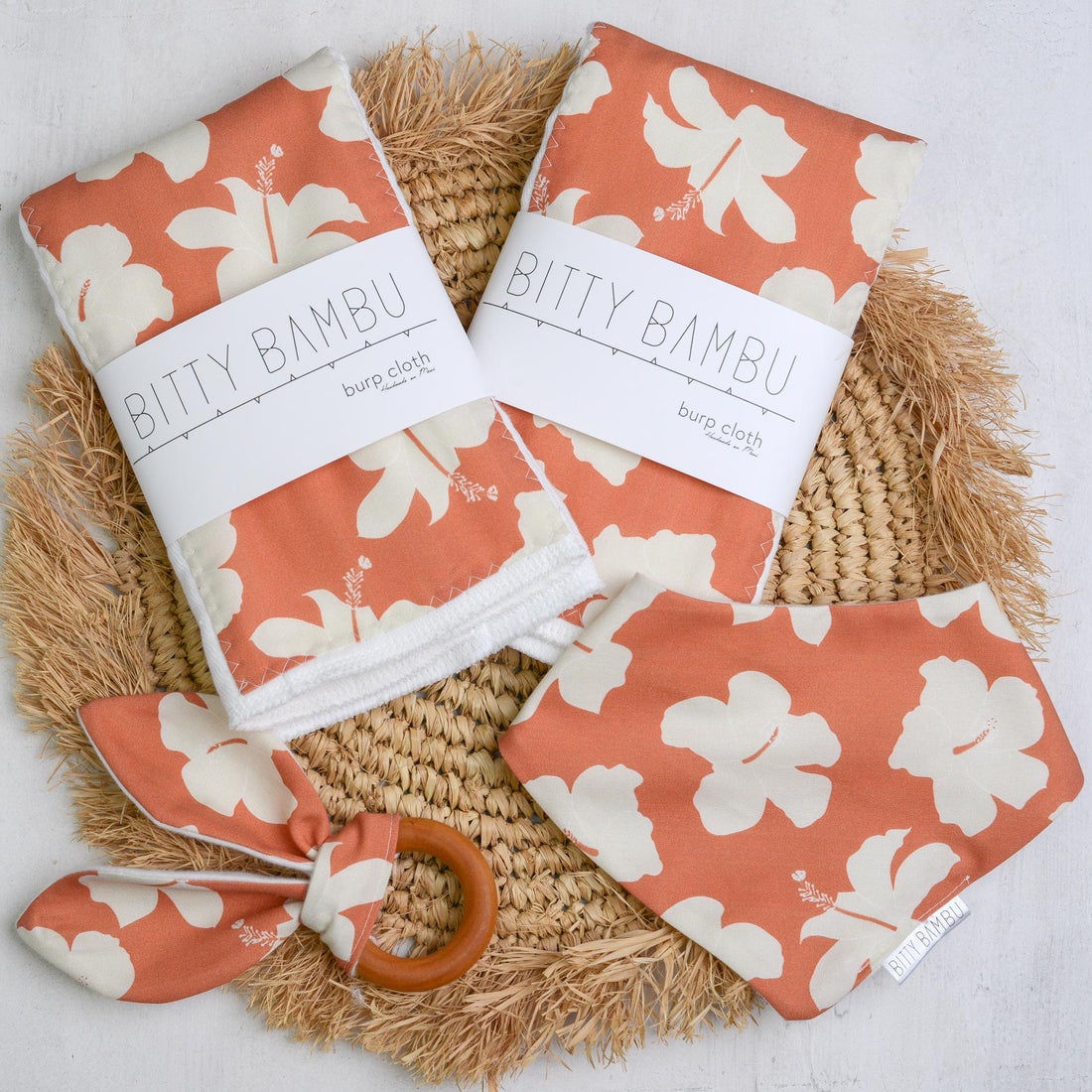 Bitty Bambu baby bibs with floral pattern on a woven mat