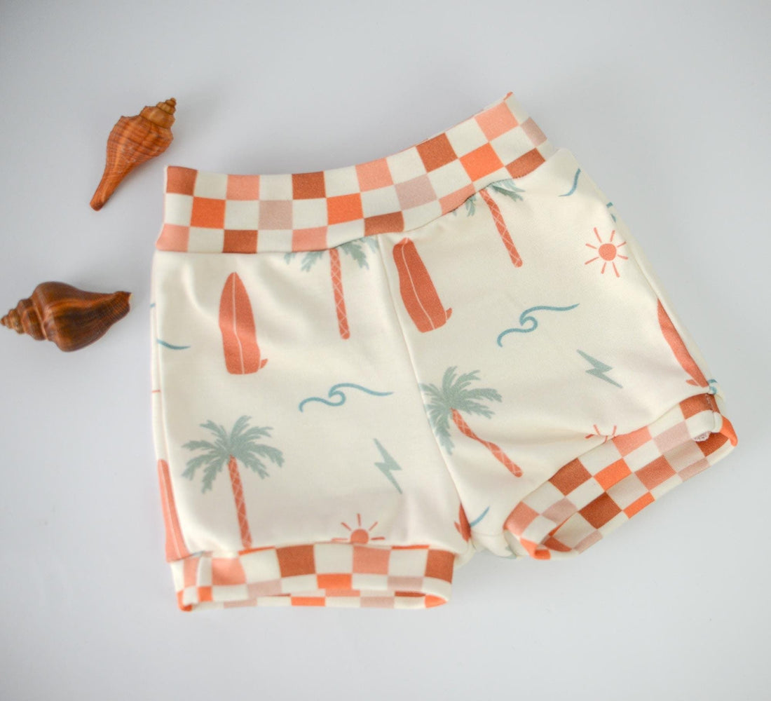 Organic knit shorts shown layed flat featuring surfer design with check patterned trim