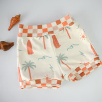 Organic knit shorts shown layed flat featuring surfer design with check patterned trim